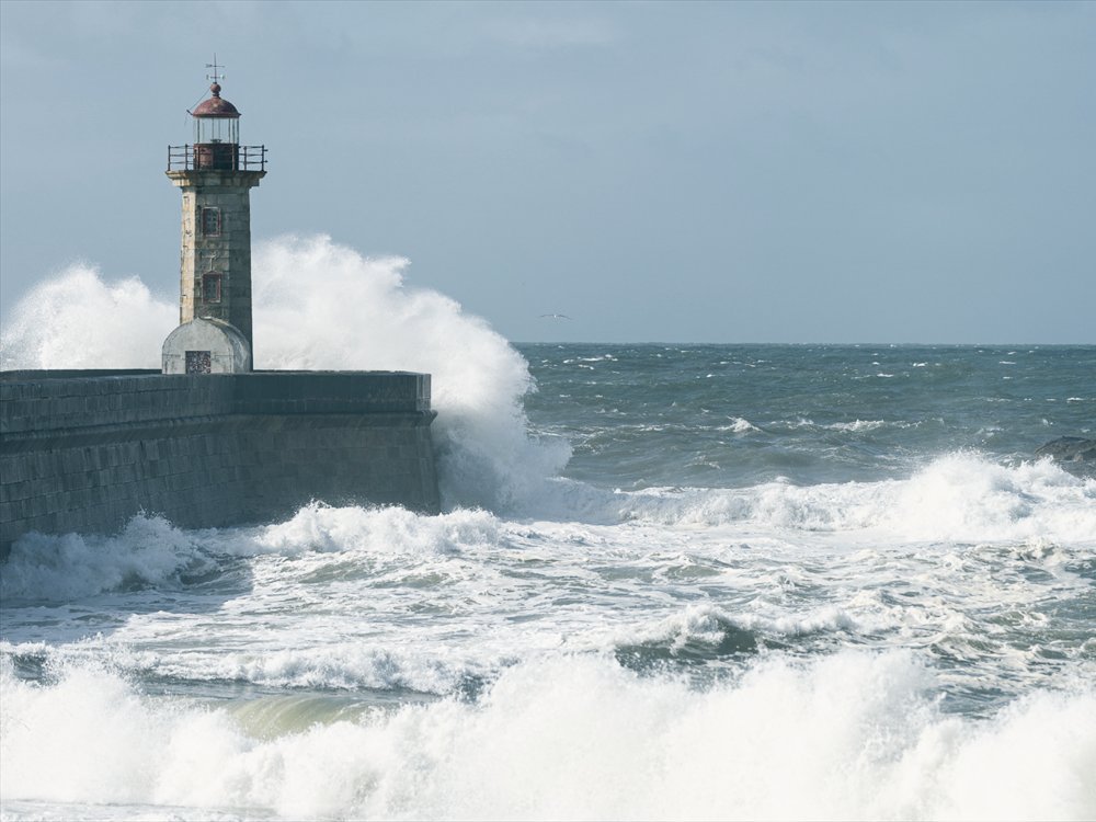 A stone lighthouse standing firm as a wave breaks against the pier.