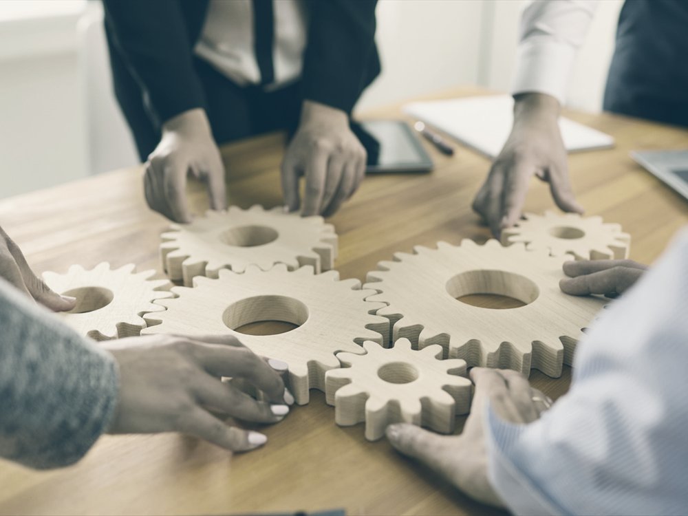 Colleagues fitting wooden cogs together on a table.